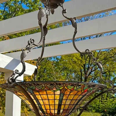 Sale Photo Thumbnail #293: Tiffany-style inverted bowl pendant chandelier featuring colorful leaded stained glass with intricate scrollwork bronze-tone hardware.
