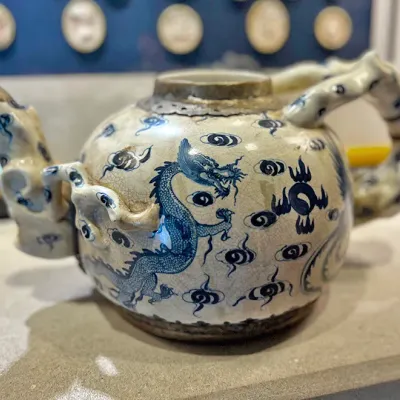 Sale Photo Thumbnail #5: Antique Asian ceramic teapot featuring hand-painted blue dragon and cloud motifs over a crackle glaze background, with a metallic-trimmed rim and sculpted handles.