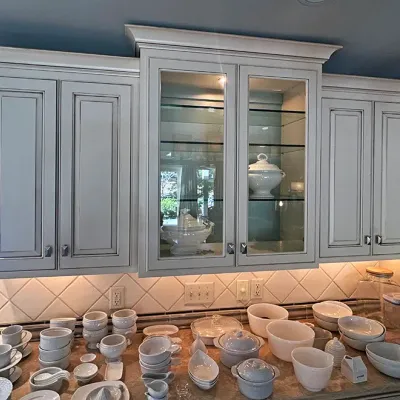Sale Photo Thumbnail #50: Collection of white ceramic kitchenware and serveware, including bowls, cups, ramekins, and turingers, displayed on a kitchen counter beneath off-white cabinetry.
