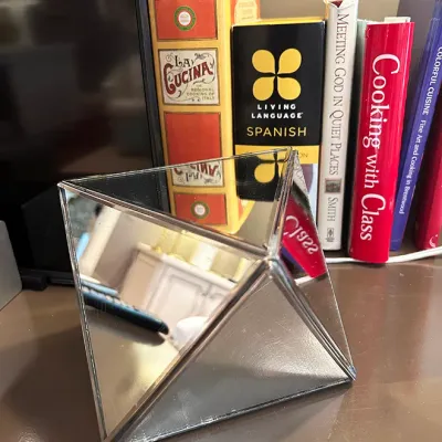 Sale Photo Thumbnail #72: Geometric mirrored glass pyramid decorative object displayed on a table alongside a collection of books.