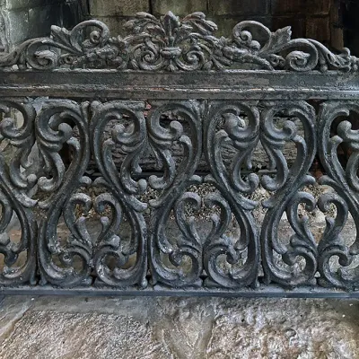 Sale Photo Thumbnail #116: Ornate cast iron fireplace fender featuring intricate scrollwork and a fleur-de-lis crest ornament.