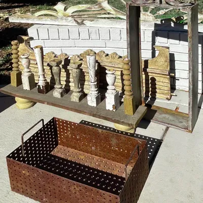 Sale Photo Thumbnail #248: Assortment of rustic architectural salvage items, including a perforated metal crate, carved wooden spindle candlesticks on a bench, and a wrought iron framed structure.