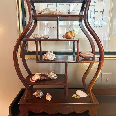 Sale Photo Thumbnail #149: Vintage Asian-style wooden display stand featuring asymmetric shelving, filled with a collection of decorative seashells.