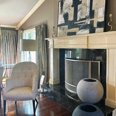Sale Photo Thumbnail #2: Large abstract textured canvas wall art mounted above a traditional white fireplace mantle with dark marble surround, alongside a modern patterned armchair and spherical floor vases.