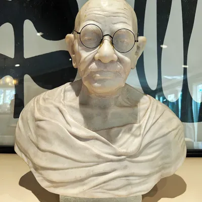 Sale Photo Thumbnail #65: Carved stone or marble bust depicting Mahatma Gandhi wearing round wire-rimmed spectacles, set on a low rectangular base.