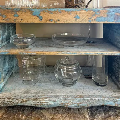 Sale Photo Thumbnail #115: Rustic wooden console shelf with heavily distressed blue painted finish, holding various clear glass serveware and decor pieces.