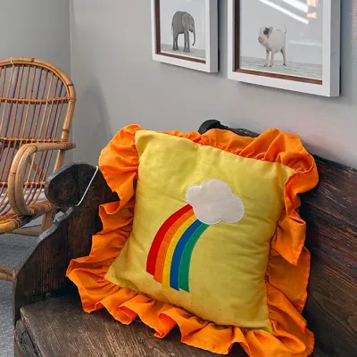 Sale Photo Thumbnail #23: Vintage 1970s yellow accent pillow featuring a rainbow and cloud applique with an orange ruffled border, displayed on a rustic wooden bench.