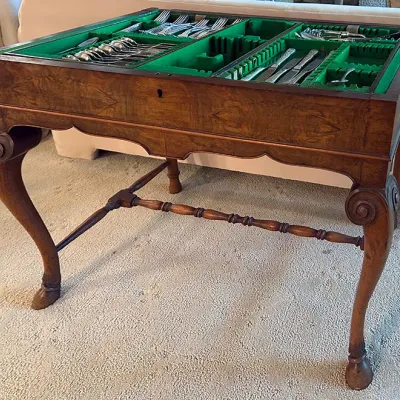Sale Photo Thumbnail #129: Antique carved wood silverware canteen table featuring cabriole legs with pad feet, a turned stretcher, and a green felt-lined interior storage compartment filled with flatware.