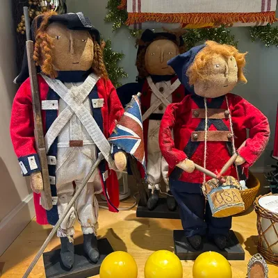 Sale Photo Thumbnail #86: Trio of handmade Revolutionary War-themed cloth folk art dolls on wooden display bases, shown alongside three bright yellow spherical candles.