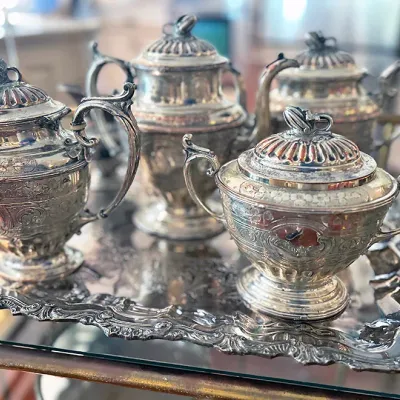 Sale Photo Thumbnail #107: Vintage silver-plated tea service set with intricate floral scrollwork engraving, including a teapot, coffee pot, creamer, sugar bowl, and matching serving tray.