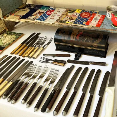 Sale Photo Thumbnail #282: Collection of vintage bone and wood-handled flatware laid out beside vintage cookbooks and a decorative black painted box.