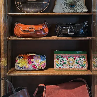 Sale Photo Thumbnail #161: Collection of designer and vintage handbags displayed on cabinet shelves, including a Louis Vuitton Loop crescent bag, patent leather Coach shoulder bags, floral embroidered clutches, and a Coach suede crossbody bag.