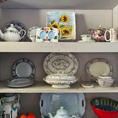 Sale Photo Thumbnail #274: Collection of decorative ceramics and tableware displayed on painted hutch shelves, including transferware platters, a tea service, hand-painted Majolica-style pieces, and a jack-o'-lantern container.