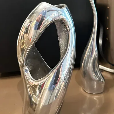 Sale Photo Thumbnail #70: Two polished chrome or silver-tone modern decor pieces, including an abstract hollowed sculpture and an elongated stylized bird figurine.