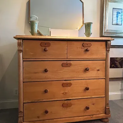Sale Photo Thumbnail #186: Antique pine chest of drawers featuring keyhole escutcheons, wooden knobs, and turned bun feet, topped with an octagonal framed wall mirror.