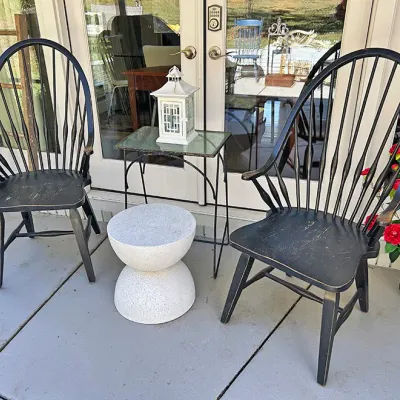 Sale Photo Thumbnail #249: Pair of distressed black painted Windsor-style armchairs displayed outdoors alongside small accent tables.