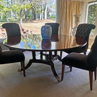 Sale Photo Thumbnail #144: Polished dark wood round dining table with brass caster feet, paired with four black button-tufted upholstered dining chairs.