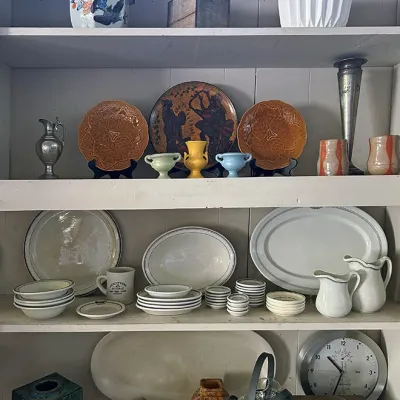 Sale Photo Thumbnail #275: Shelves displayed with vintage ceramic dishware, art pottery, serving platters, decor pieces, and a round wall clock.