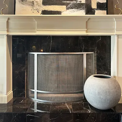 Sale Photo Thumbnail #83: Contemporary fireplace set featuring a curved brushed metal fire screen, dark marble tiled hearth and surround, a cream-painted mantel, and a large spherical stone vessel.
