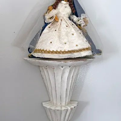 Sale Photo Thumbnail #31: Vintage Madonna and Child doll figure clad in elaborate lace and velvet robes, displayed on a distressed white fluted wall sconce shelf.
