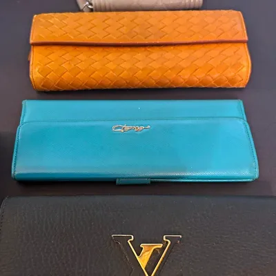 Sale Photo Thumbnail #160: Collection of four designer leather wallets including a black Louis Vuitton Capucines wallet, teal continental wallet, woven tan leather flap wallet, and beige quilted zip wallet.