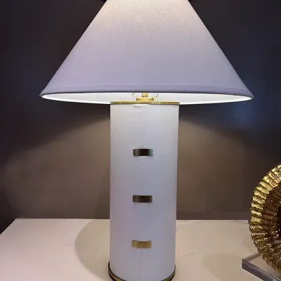 Sale Photo Thumbnail #67: Modern white cylindrical table lamp featuring faux leather wrapping with stitched seam detail, brass metallic tabs, and a white fabric shade.