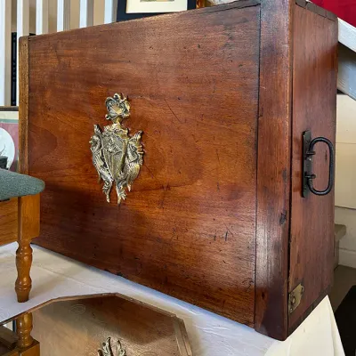 Sale Photo Thumbnail #278: Vintage wooden chest with an ornate brass crest, side metal handles, and minor surface wear.