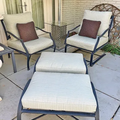 Sale Photo Thumbnail #241: Outdoor patio seating set featuring dark metal frames, light gray cushions, brown patterned accent pillows, and matching ottomans.