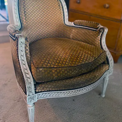 Sale Photo Thumbnail #146: French Louis XVI style armchair featuring a distressed whitewashed wooden frame with carved guilloche detailing and patterned upholstery.