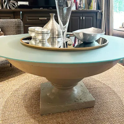 Sale Photo Thumbnail #39: Contemporary round frosted glass coffee table supported by a stone-look urn-style pedestal base, styled with decorative metal bowls and glassware.
