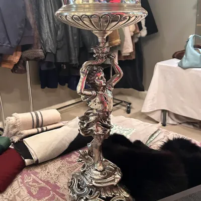 Sale Photo Thumbnail #155: Ornate silver-plated figural compote, featuring a sculpted cherub pedestal base supporting a gadrooned bowl.