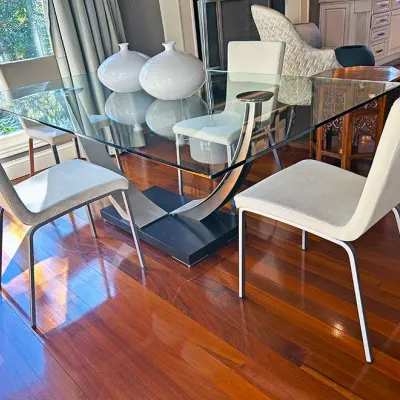Sale Photo Thumbnail #76: Modern glass-top dining table set featuring a sculpted chrome and black base, accompanied by four light gray upholstered side chairs with metal legs.