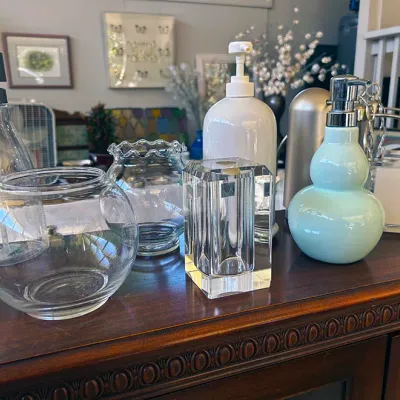 Sale Photo Thumbnail #265: Collection of modern bath accessories and glassware displayed on a wooden surface, including light blue and white liquid soap dispensers, a heavy crystal vase, and clear glass bowls.