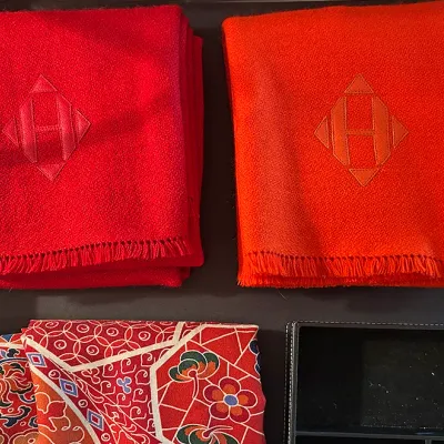Sale Photo Thumbnail #159: Pair of Hermès fringed cashmere throw blankets in red and orange featuring the signature geometric 'H' monogram embroidery, displayed with a patterned silk scarf.