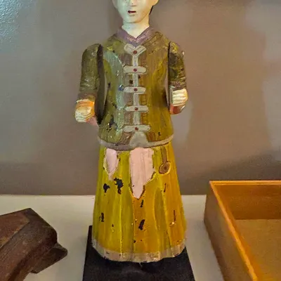Sale Photo Thumbnail #101: Hand-carved and painted wooden folk art figure depicting a person in traditional Asian attire, mounted on a black wooden display base.