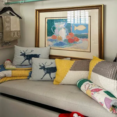 Sale Photo Thumbnail #21: Upholstered storage bench styled with throw pillows, folded quilts, and a framed still life print, with shelf storage visible above.