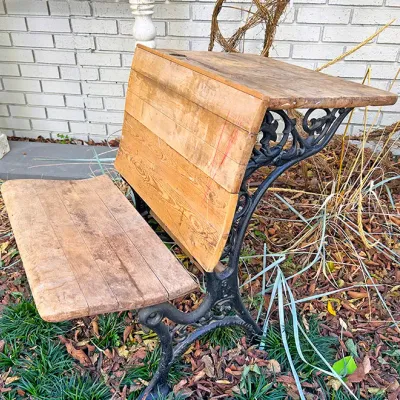 Sale Photo Thumbnail #246: Antique wooden and ornate cast iron school desk with attached bench seat, featuring a natural wood finish and inkwell hole.