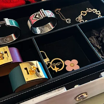 Sale Photo Thumbnail #254: Collection of designer jewelry and accessories displayed in a black felt-lined tray, including an Hermès Clic Clac H bracelet, Kelly leather cuff bracelets, and a Louis Vuitton flower charm.
