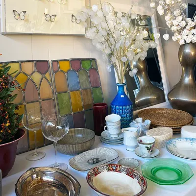 Sale Photo Thumbnail #285: Collection of tabletop decor and home goods including stained glass panels, framed butterfly specimens, silver-plated serving pieces, ceramic bowls, glass stems, and decorative vases.