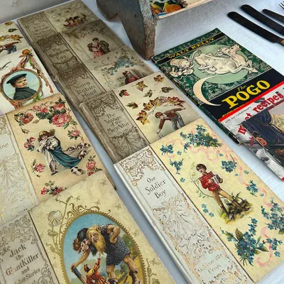 Sale Photo Thumbnail #257: Collection of antique children's books with decorative cloth covers alongside vintage Walt Kelly comic books and cookbooks.