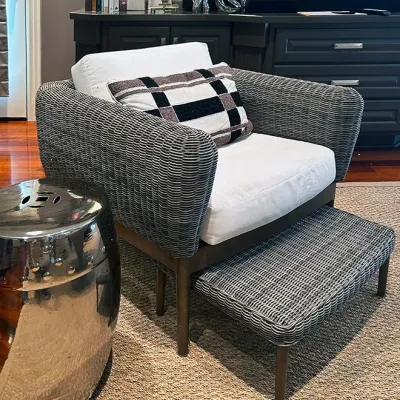 Sale Photo Thumbnail #38: Modern woven outdoor-style armchair with matching ottoman, white upholstery cushions, and a patterned throw pillow. Includes a metallic chrome garden stool in the foreground.