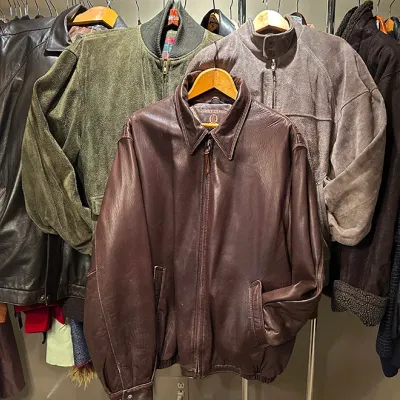 Sale Photo Thumbnail #294: Collection of men's vintage leather and suede bomber jackets hanging on a clothing rack, including brown leather and green suede styles.