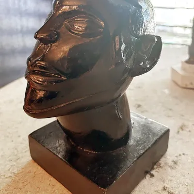 Sale Photo Thumbnail #12: Black glazed ceramic head bust sculpture mounted on a square pedestal base, featuring stylized mid-century art deco features.