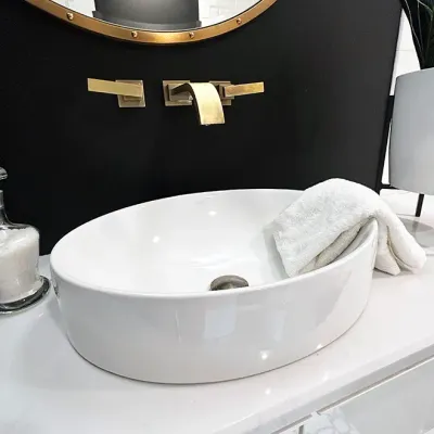 Sale Photo Thumbnail #181: Modern Kohler oval ceramic vessel sink mounted on a white countertop, featuring a wall-mounted brushed brass faucet and hardware set.
