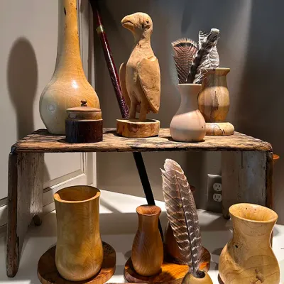 Sale Photo Thumbnail #55: Collection of hand-turned wooden vases, bowls, and a carved bird figurine arranged on a rustic wooden riser.