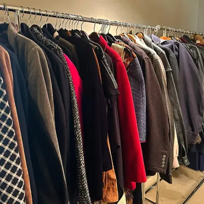 Sale Photo Thumbnail #170: A metal clothing rack filled with an assortment of vintage coats, jackets, and sweaters in various colors and fabrics.