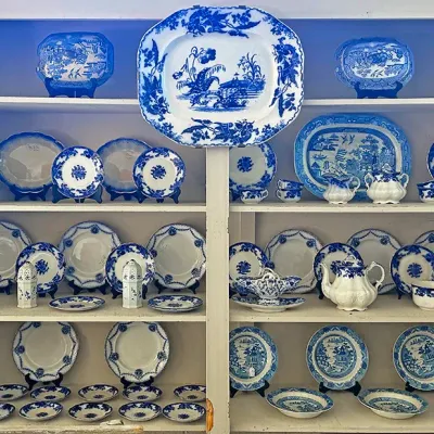 Sale Photo Thumbnail #255: Collection of vintage blue and white transferware china, including serving platters, teapot, sugar bowl, salt and pepper shakers, and various plates arranged in a white built-in cabinet.
