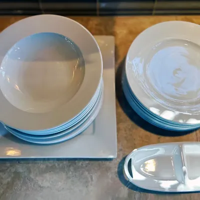 Sale Photo Thumbnail #43: Set of modern white porcelain dishware, including stacks of wide-rimmed soup bowls, dinner plates, square charger plates, and a divided serving dish.