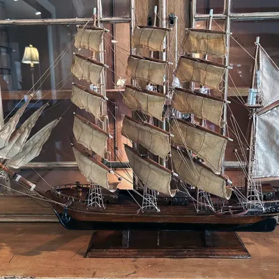 Sale Photo Thumbnail #126: Detailed vintage wooden model of a three-masted tall ship, featuring cloth sails, intricate rigging, and a wooden display stand.