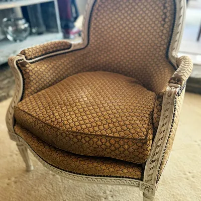 Sale Photo Thumbnail #110: French Provincial style armchair featuring a carved whitewashed wood frame and patterned gold and brown upholstery with nailhead trim.